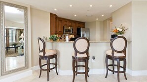 A kitchen with three wooden bar stools, a large mirror, and a countertop with kitchen appliances. - Private Villa 1980 (Kissimmee)