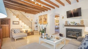 A spacious living room with a high ceiling, wooden beams, a fireplace, a flat-screen TV, and a staircase leading to another level. - Sa Teulera by Interhome (Campanet)