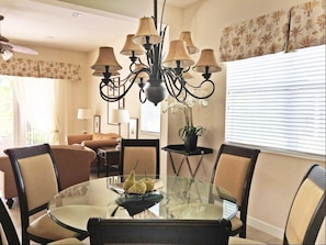 A dining area with a glass table surrounded by chairs, a chandelier, and a potted plant.