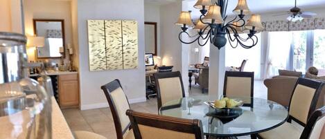 A dining area with a round glass table, six chairs, and a chandelier.