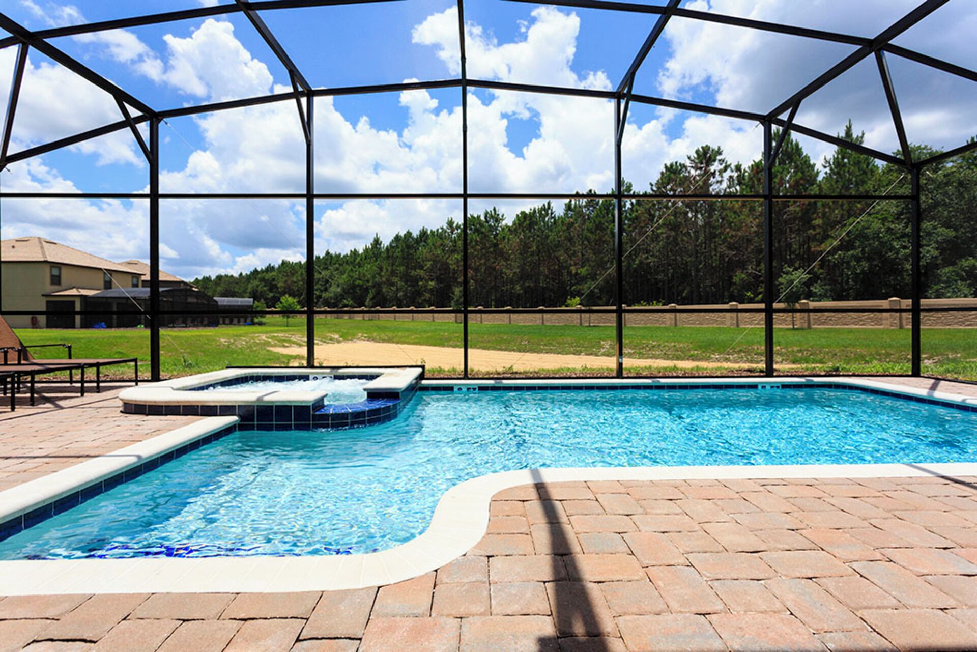 Piscina com hidromassagem, cercada por um terraço coberto com piso de tijolos.