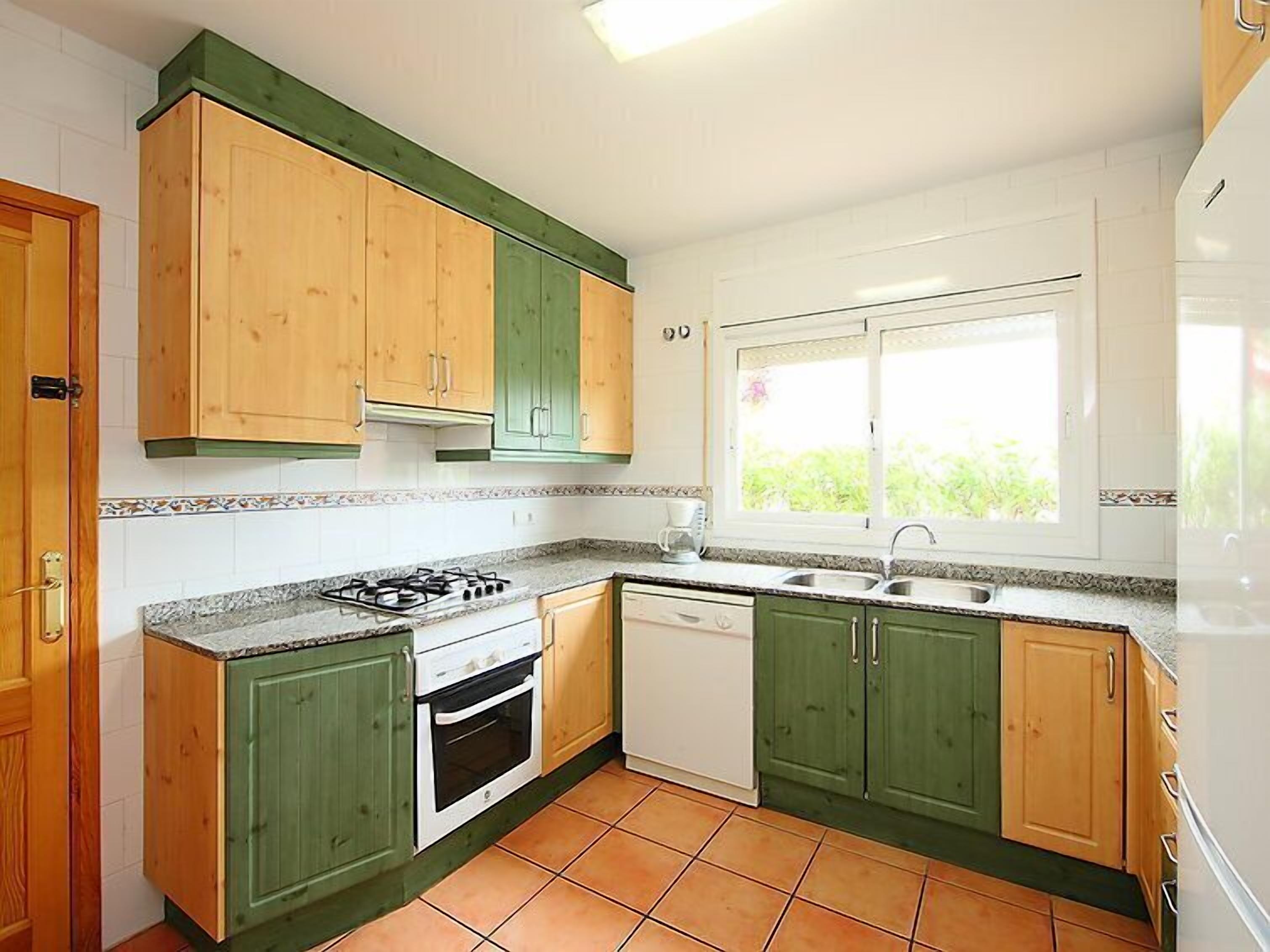 A kitchen with green and wooden cabinets, a gas stove, a dishwasher, and a window providing natural light.