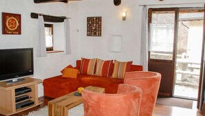 Una sala de estar con un sofá rojo, una mesa de centro de madera y un televisor sobre un mueble de madera. Hay una puerta corrediza de vidrio que da al exterior.