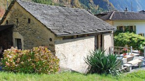 Un edificio de piedra con techo inclinado, rodeado por un jardín con diversas plantas y un pequeño cementerio.