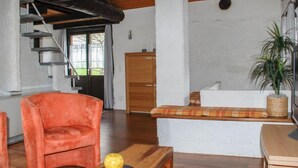 Una sala de estar acogedora con techo de madera, un sofá, un sillón, una mesa de madera con fruta y una planta en maceta.