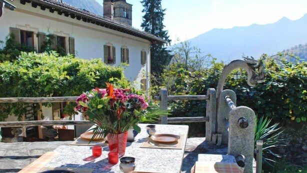 Un espacio de comedor al aire libre con una mesa lista para dos personas, un jarrón de flores y una fuente de piedra.