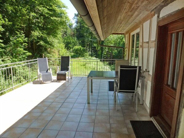 A covered outdoor area with a table and chairs, a door, and a view of greenery.