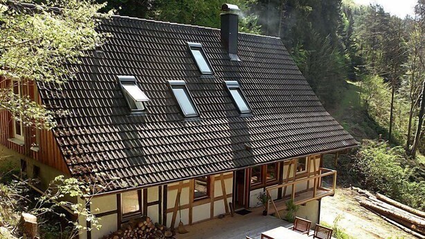 A chalet with a sloped roof, dormer windows, a wooden deck, and a view of the surrounding forest. - Leubach by Interhome (Wolfach)