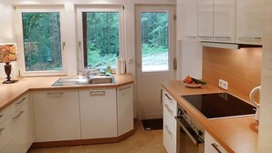 A modern kitchen with white cabinets, a built-in oven, and a large window providing a view of the forest. - Leubach by Interhome (Wolfach)