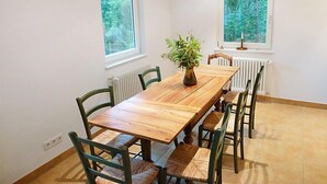 A dining room with a wooden table and chairs, a vase with flowers, and two windows with a view of trees. - Leubach by Interhome (Wolfach)