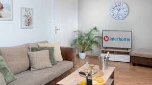 Un soggiorno con un divano marrone, un tavolino in legno con una bottiglia di champagne, un telecomando e un televisore che mostra il logo Interhome.