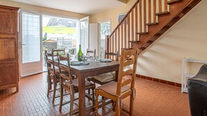 Een eetruimte met een houten tafel en stoelen, een trap en uitzicht op het buiten.