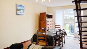 Een eethoek met een tafel voor vier personen, een houten kast met decoratieve deuren, een zwarte leren bank en een schilderij aan de muur.