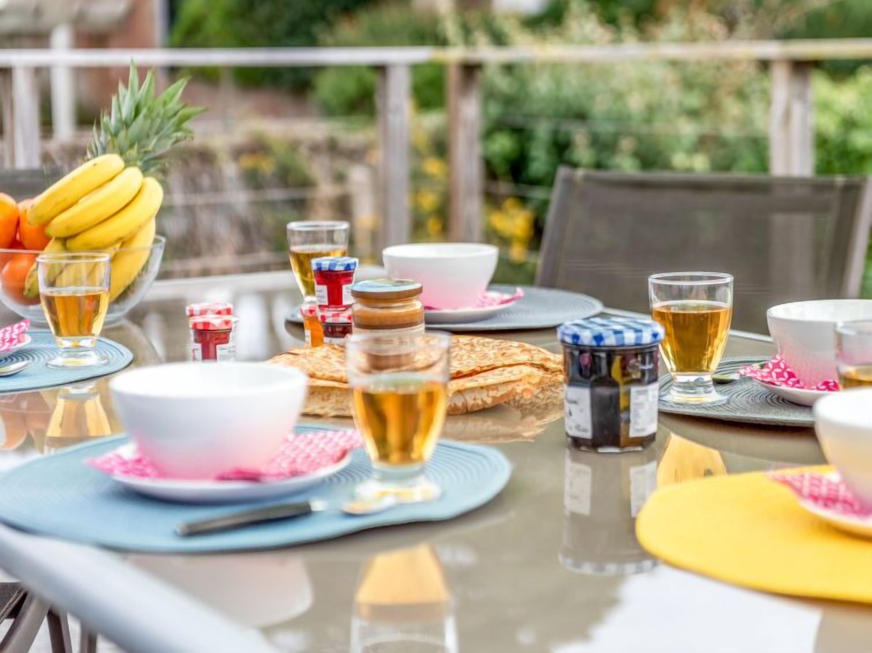 An outdoor dining area with a table set for breakfast, including fruits, bread, and beverages.