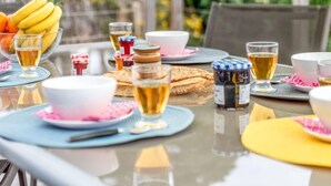 Een buitenontbijtplaats met een gedekte tafel, inclusief fruit, brood en drankjes.