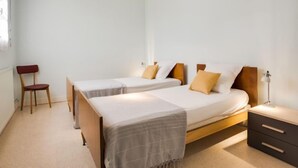 Een slaapkamer met twee eenpersoonsbedden, een stoel, een nachtkastje en een hanglamp.