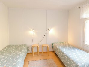 Una habitación con dos camas individuales, un taburete de madera, un tapete tejido y una lámpara fijada a la pared.