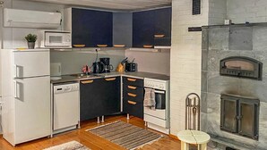 A compact kitchen with white appliances, dark cabinets, and a stone fireplace.