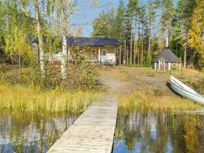 A wooden dock leading to a house with a porch, surrounded by tall trees and a small boat. - Hiekkalampi by Interhome (Kontiolahti)
