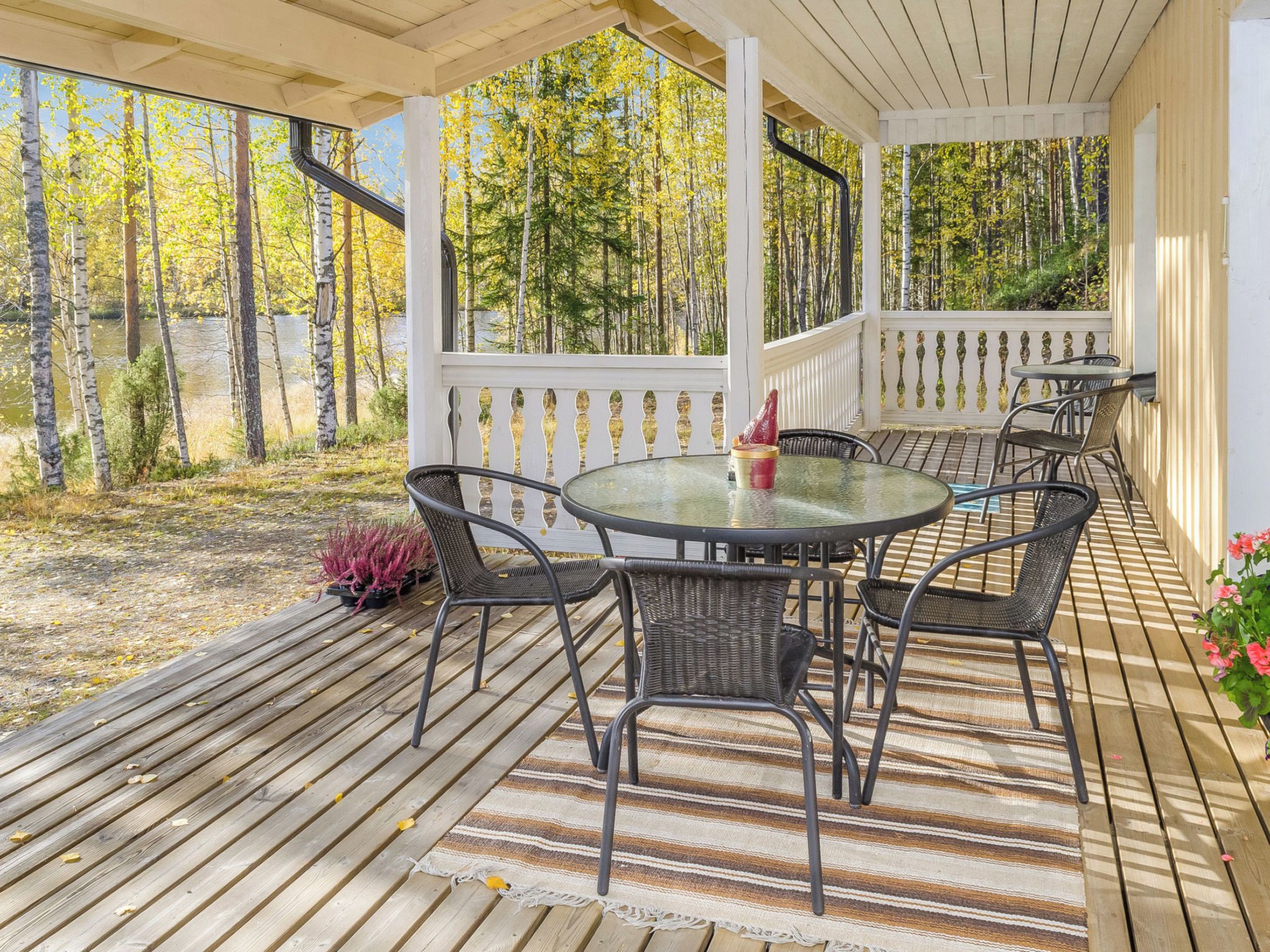 Un espace extérieur abrité, aménagé avec une table ronde et des chaises, entouré d’une terrasse en bois et d’une rambarde.