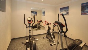 Une salle de remise en forme équipée de machines de cardio, d’un miroir et de posters aux murs.
