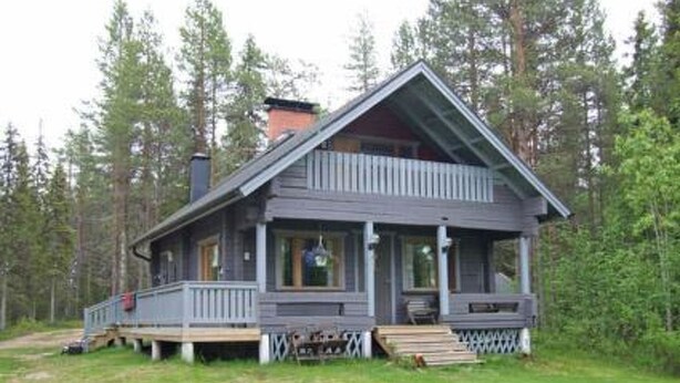 A two-story cabin with a porch, surrounded by trees.
