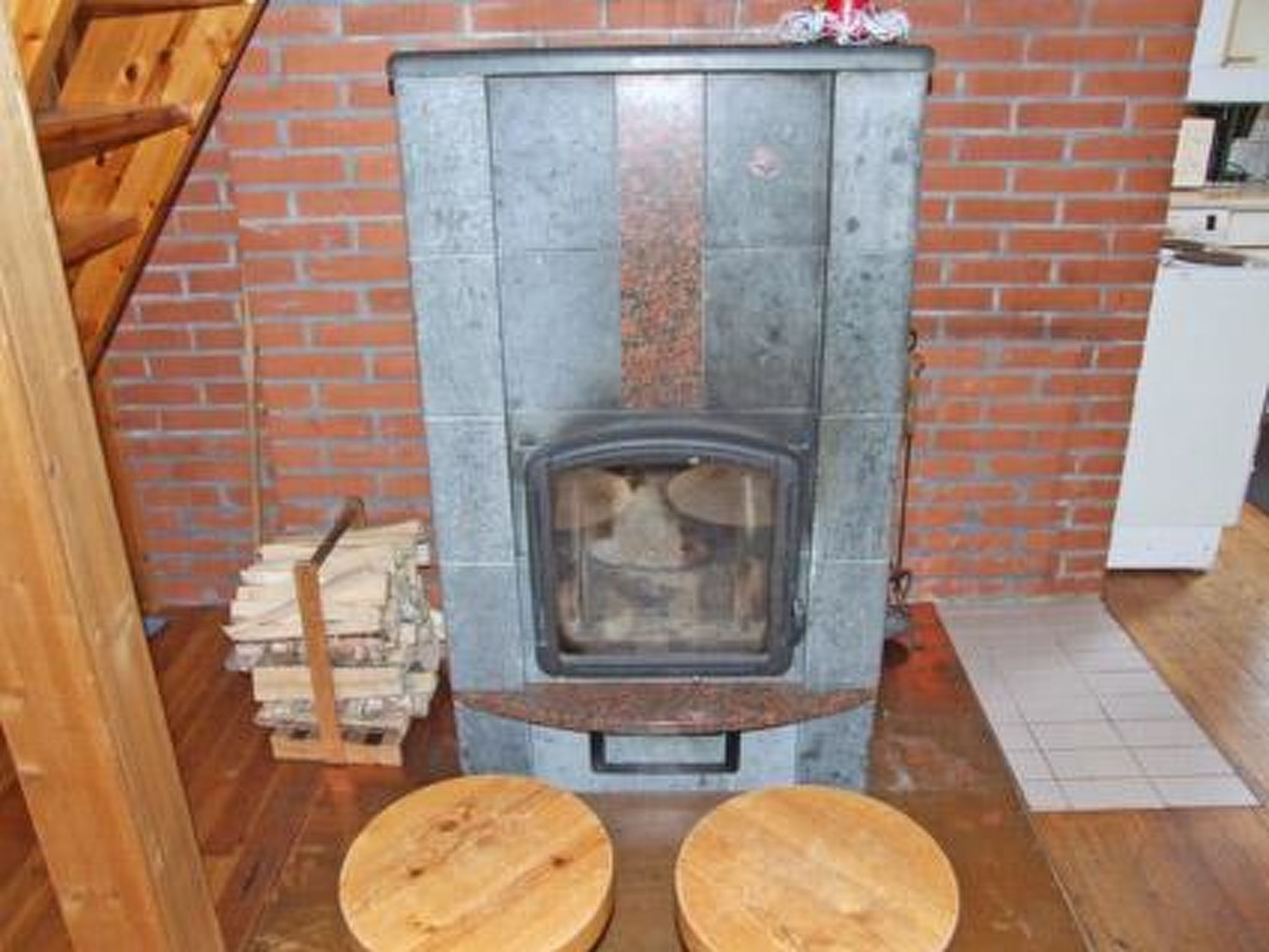 A rustic room with a brick wall, a wood-burning stove, and two wooden stools.