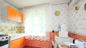 Eine Küche mit orangefarbenen Schränken, einer Ziegelrückwand, einem Fenster mit Spitzenvorhang, einer Kaffeemaschine und einem Toaster.