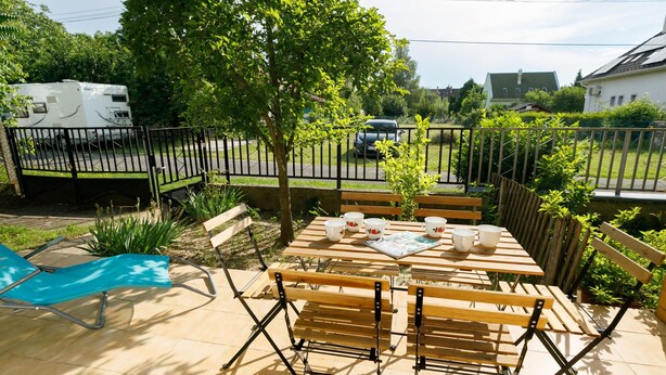 Eine Terrasse im Freien mit einem Holztisch, gedeckt für vier Personen, umgeben von hölzernen Bänken.
