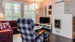 Una sala de estar acogedora con un sillón a cuadros, un sofá rojo, un televisor de pantalla plana y una chimenea.