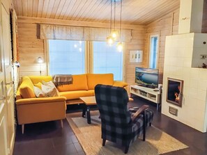 A cozy living room with a sofa, armchair, TV, fireplace, and wooden walls.