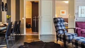 Un interior moderno con zona de comedor, un sillón a cuadros, un sofá púrpura y un reloj en la pared.