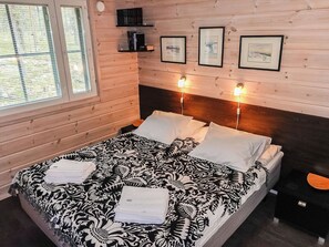 A wooden room with a bed, two shelves with books, and three framed pictures on the wall.