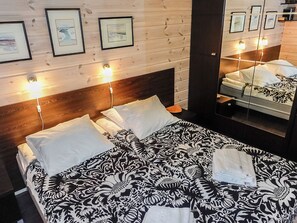 A hotel room with a wooden headboard, a large bed with patterned bedding, and wall-mounted lights. - Aarrekammi by Interhome (Inari)