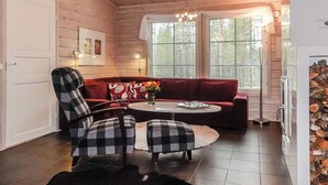 Una habitación acogedora con un sofá rojo, dos sillones a cuadros, una mesita redonda y una araña.