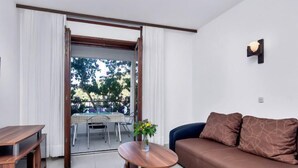 Een moderne woonkamer met een bank, een bijzettafeltje en een tv-meubel. Er is een balkon met een tafel en stoelen.