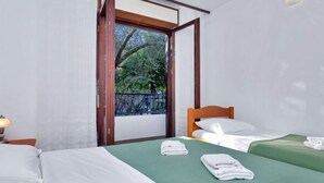Een hotelkamer met twee bedden, een raam met uitzicht op bomen en een balkon.