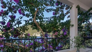 Een balkon met uitzicht op zee, overwoekerd met paarse bloemen en groen loof.