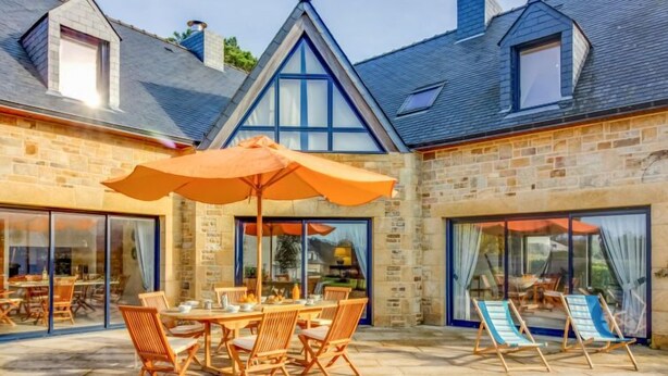 Een stenen gebouw met een patio, compleet met een tafel, stoelen, een parasol en loungestoelen.