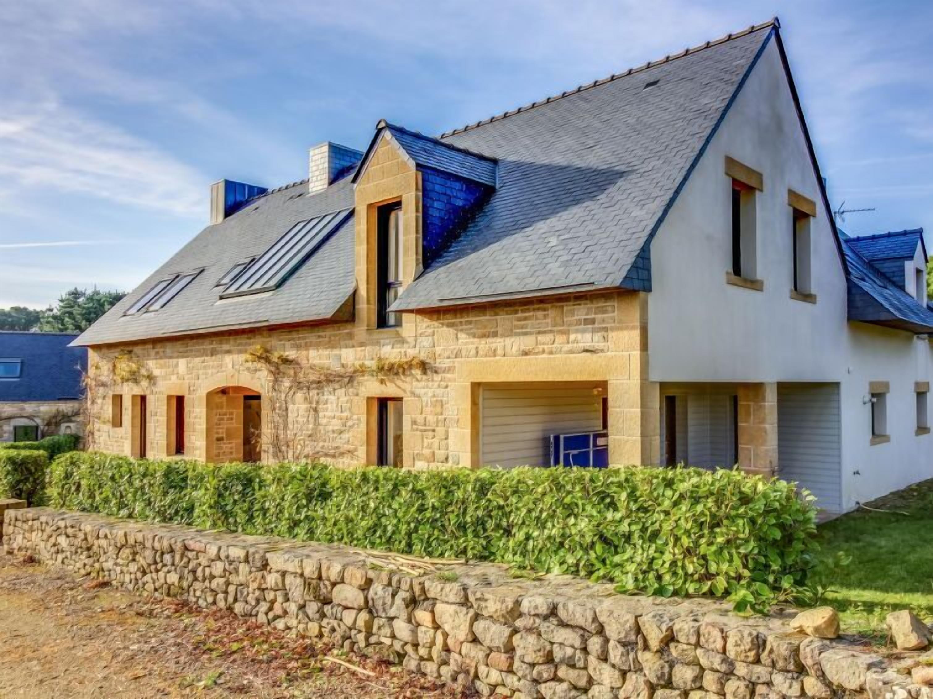 A two-story stone house with a sloped roof, a garage, and a stone wall in front.