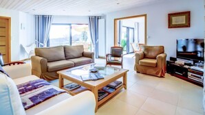 Een ruime woonkamer met houten plafond, een bank, salontafel en televisie.