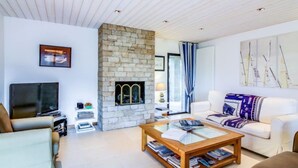 Een moderne woonkamer met een stenen open haard, een flatscreen televisie, een bank en een salontafel.