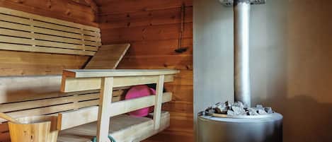 Un sauna avec des bancs en bois, une table et un appareil de sauna avec des pierres.