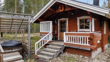 A wooden cabin with a porch, steps, and a grill area.