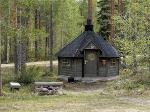 Une petite cabane dotée d’une porte hexagonale, entourée d’une forêt.