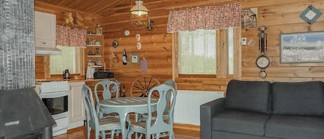 Een gezellig chaletinterieur met een eethoek, een bank, een open haard en houten wanden.