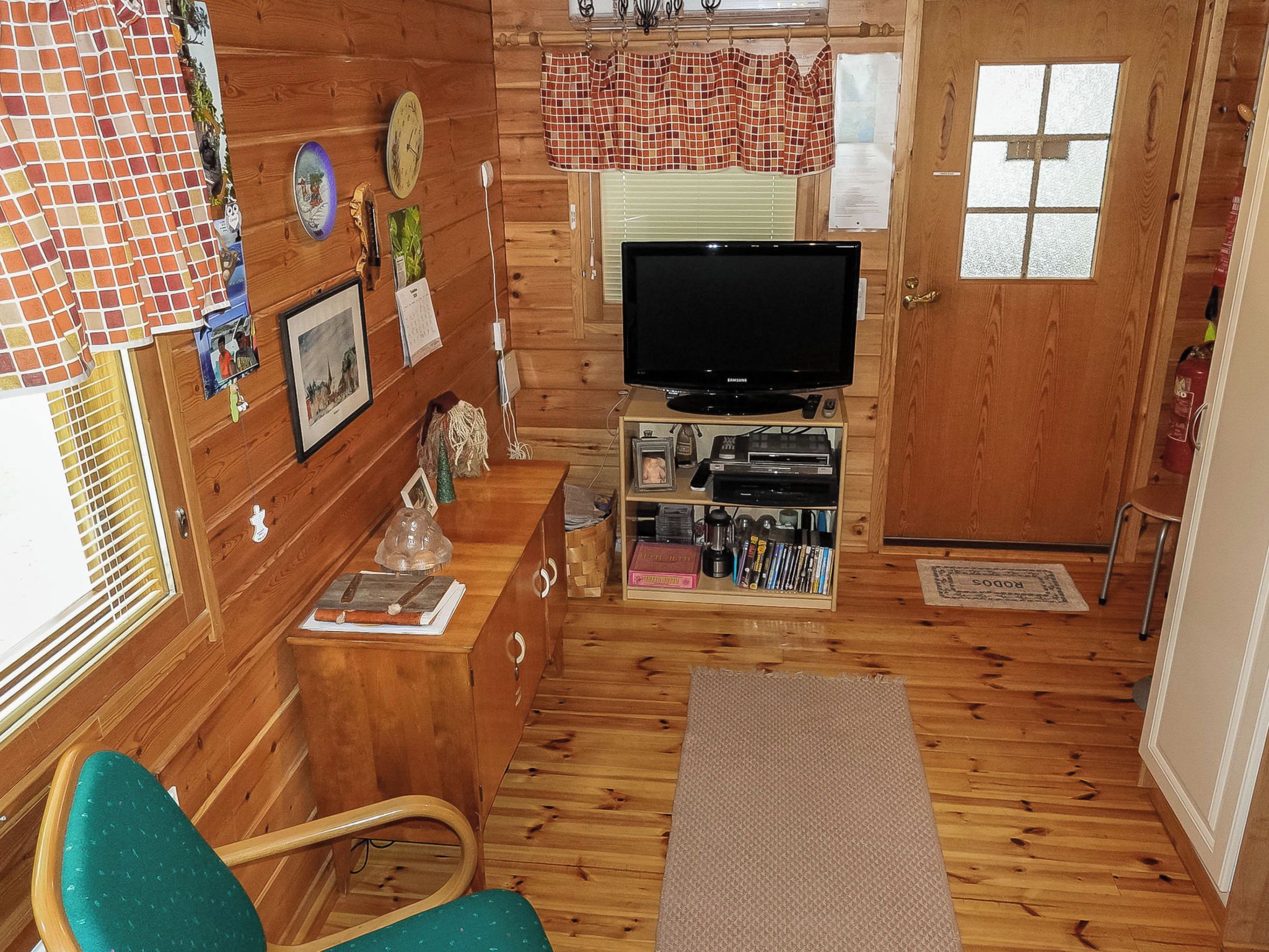 A cozy cabin interior with a television, wooden walls, a small seating area, and a door.