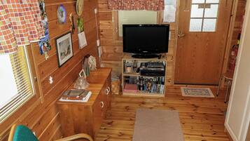 A cozy cabin interior with a television, wooden walls, a small seating area, and a door.