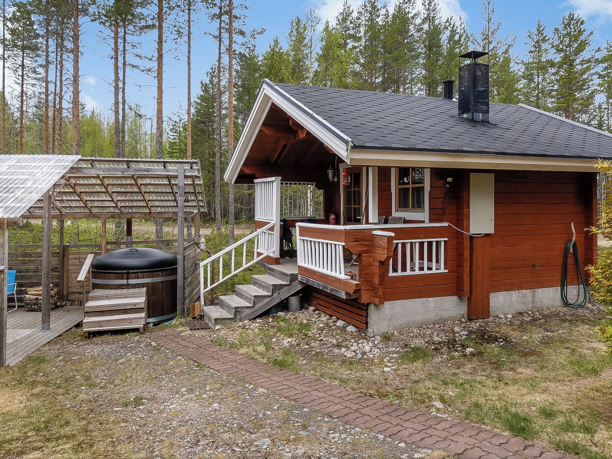 A cabin with a wooden exterior, a porch with a white railing, and a chimney.