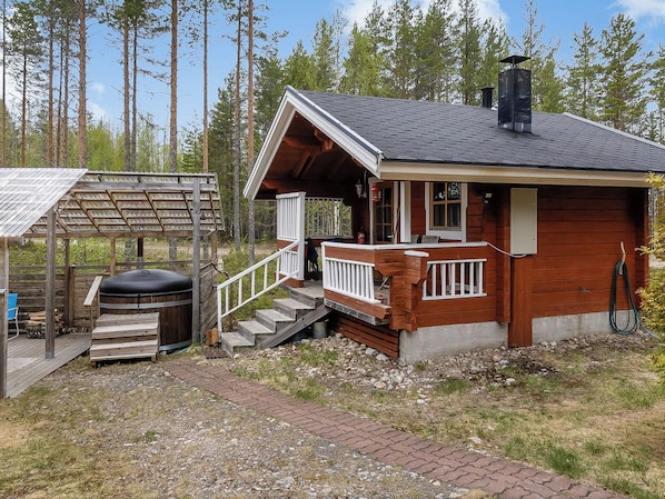 A cabin with a wooden exterior, a porch with a white railing, and a chimney.